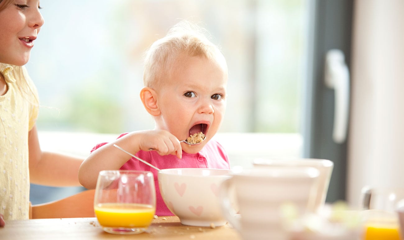 Babymädchen essen Müsli am Frühstückstisch